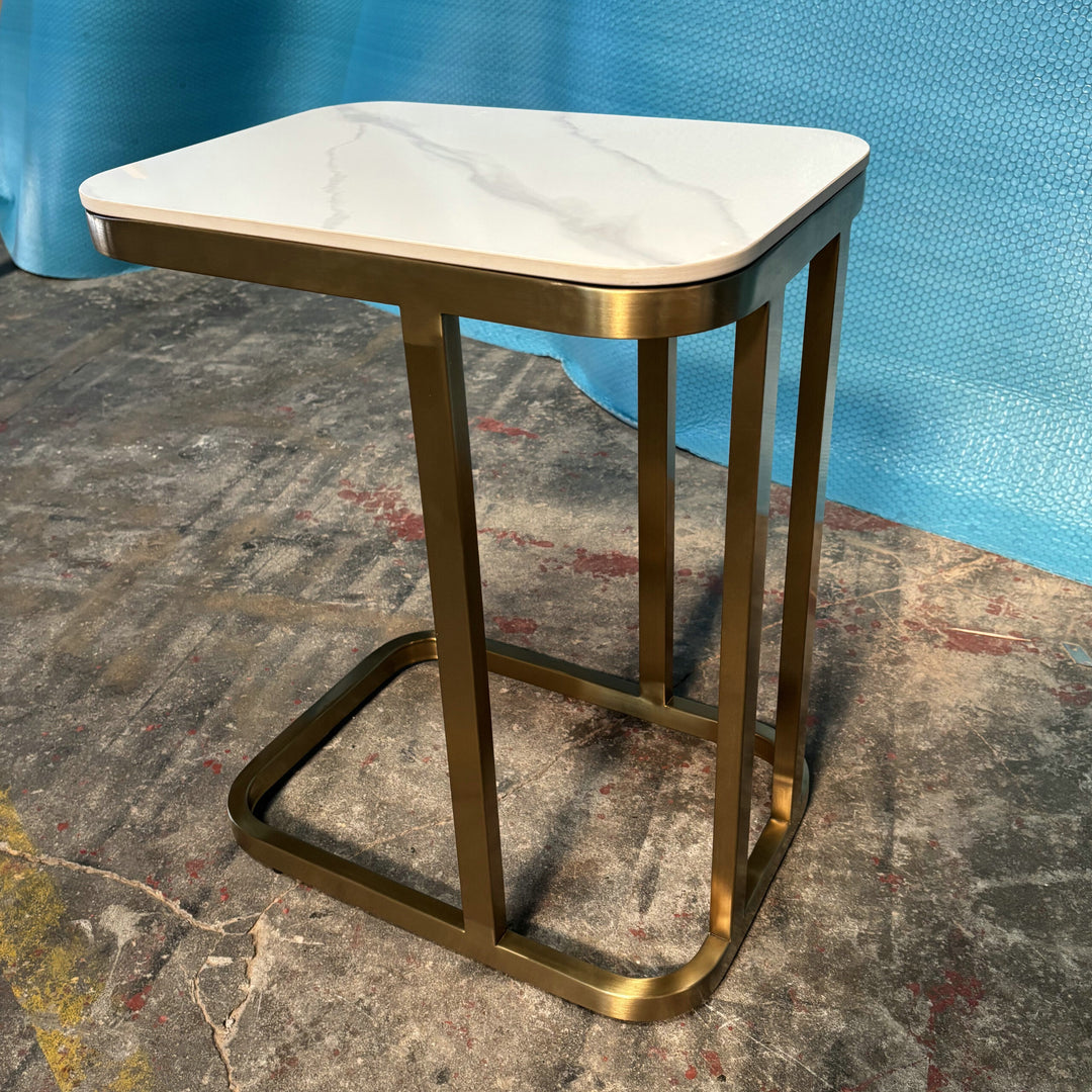 Modern accent side table with white marble top and gold metal frame on concrete floor