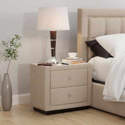 Modern beige upholstered nightstand with two drawers beside bed, lamp, and decor in bedroom