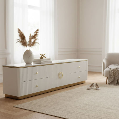 Modern white TV unit with gold accents in a bright living room, decorative vase and books on top.
