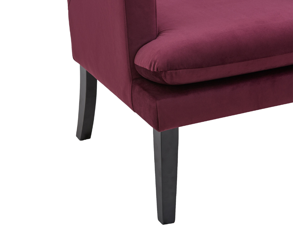Burgundy velvet upholstered chair corner with black wooden legs