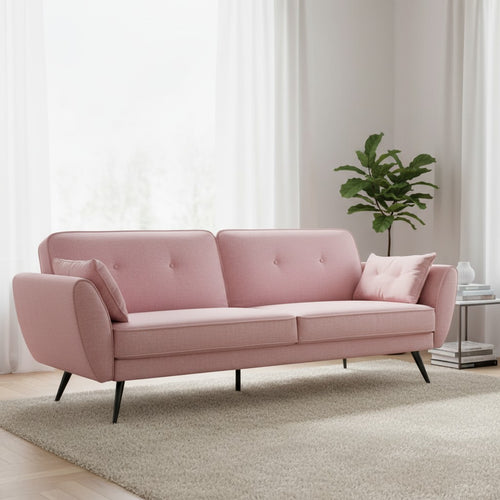 Pink mid-century modern sofa with tufted back, black legs, in bright living room with rug and plant
