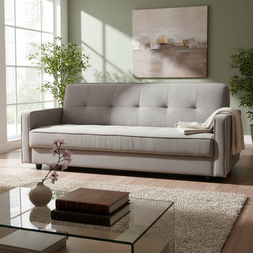 Modern gray tufted sofa in bright living room with plants, art, and glass coffee table