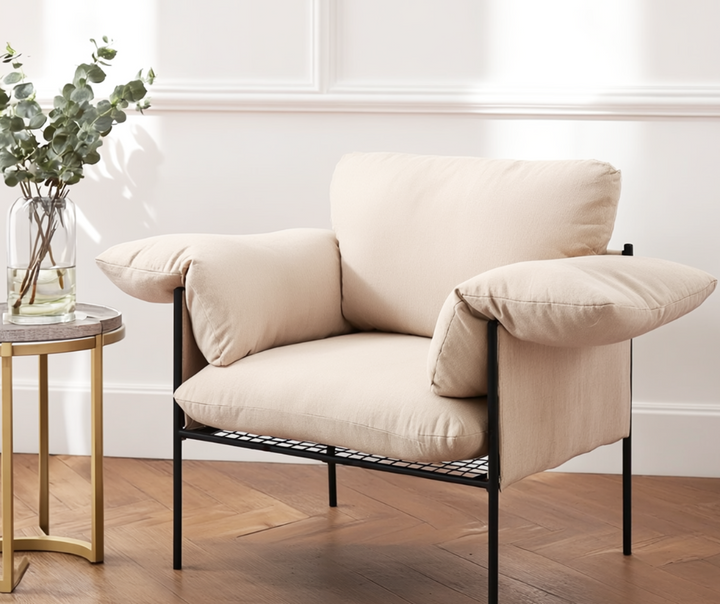 Modern beige accent armchair with plush cushions and black metal frame beside a round side table