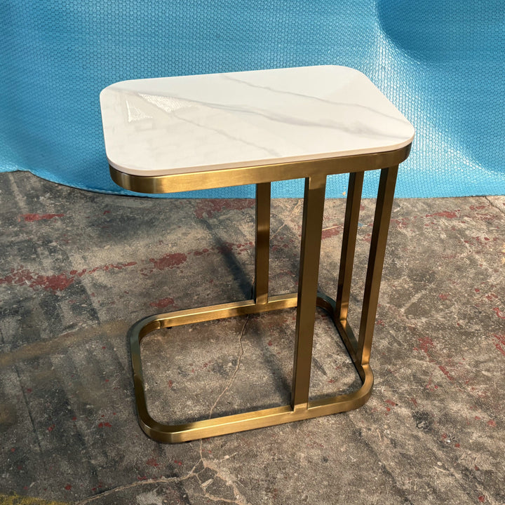Modern side table with white marble top and gold metal frame on industrial floor