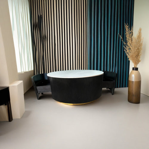 Modern round marble-top coffee table with black fluted base and gold trim, styled with dark armchairs and teal curtains