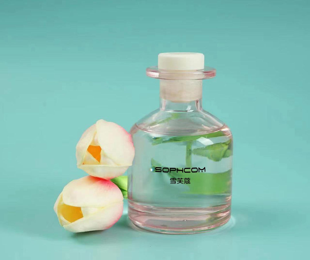 Glass fragrance diffuser bottle with floral stems and two artificial white tulip flowers on a teal background