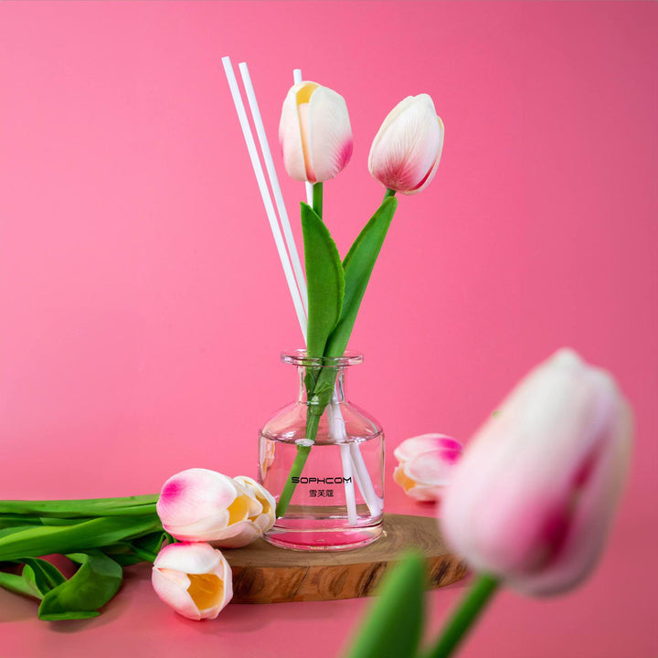 Glass vase with pink and white tulips and reed sticks on wood tray, pink background
