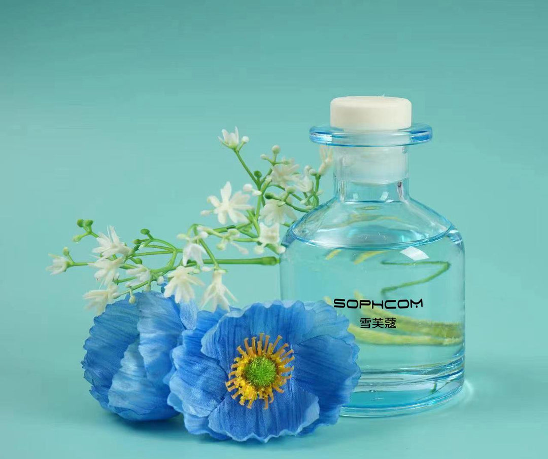 Clear glass fragrance bottle with blue artificial flowers and white blossoms on aqua background