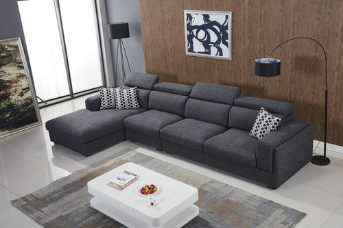 Modern grey sectional sofa with chaise lounge, patterned pillows, in stylish living room with white coffee table