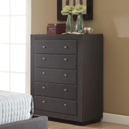 Modern gray fabric dresser with five drawers in a bedroom setting, topped with decor items
