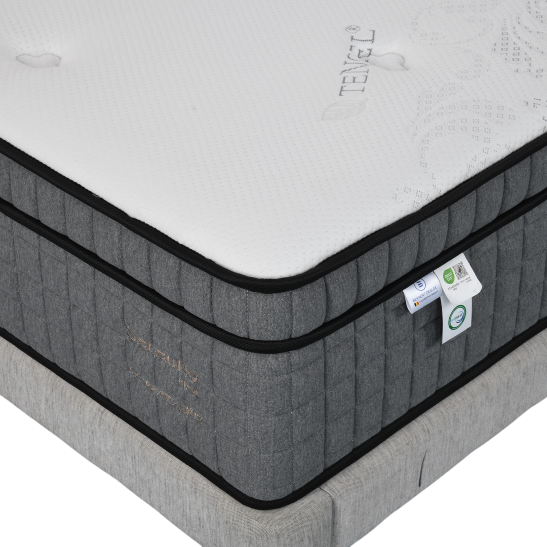 Close-up of a modern grey mattress with white top, detailed stitching, and eco-friendly labels.