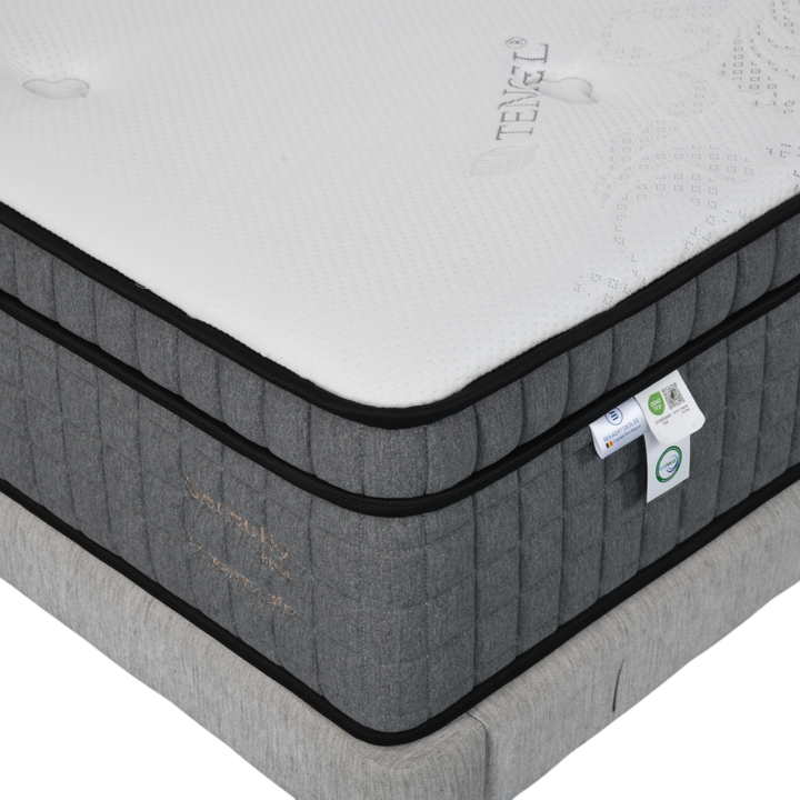 Close-up of a modern grey mattress with white top, detailed stitching, and eco-friendly labels.