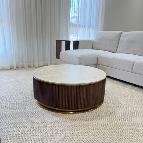 Modern round coffee table with wooden base and light top in a living room with beige sofa