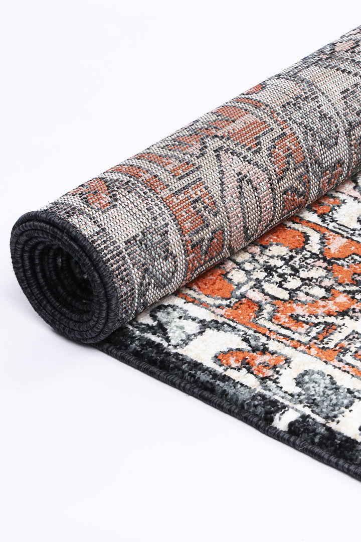 Rolled area rug with black, orange, and white geometric pattern on a white background