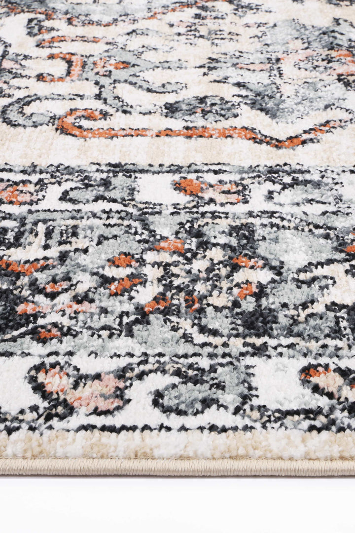 Close-up of a beige and black patterned area rug with orange accents and textured fibers.