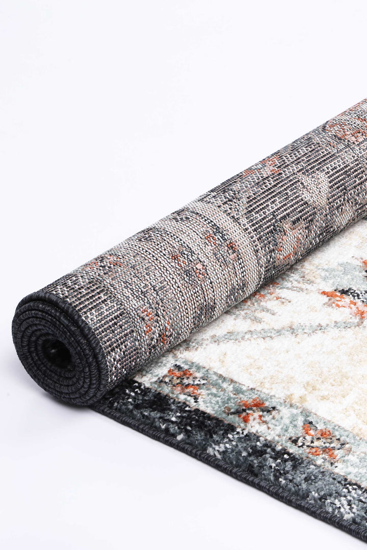 Rolled area rug with modern pattern in grey, cream, and orange tones on white background