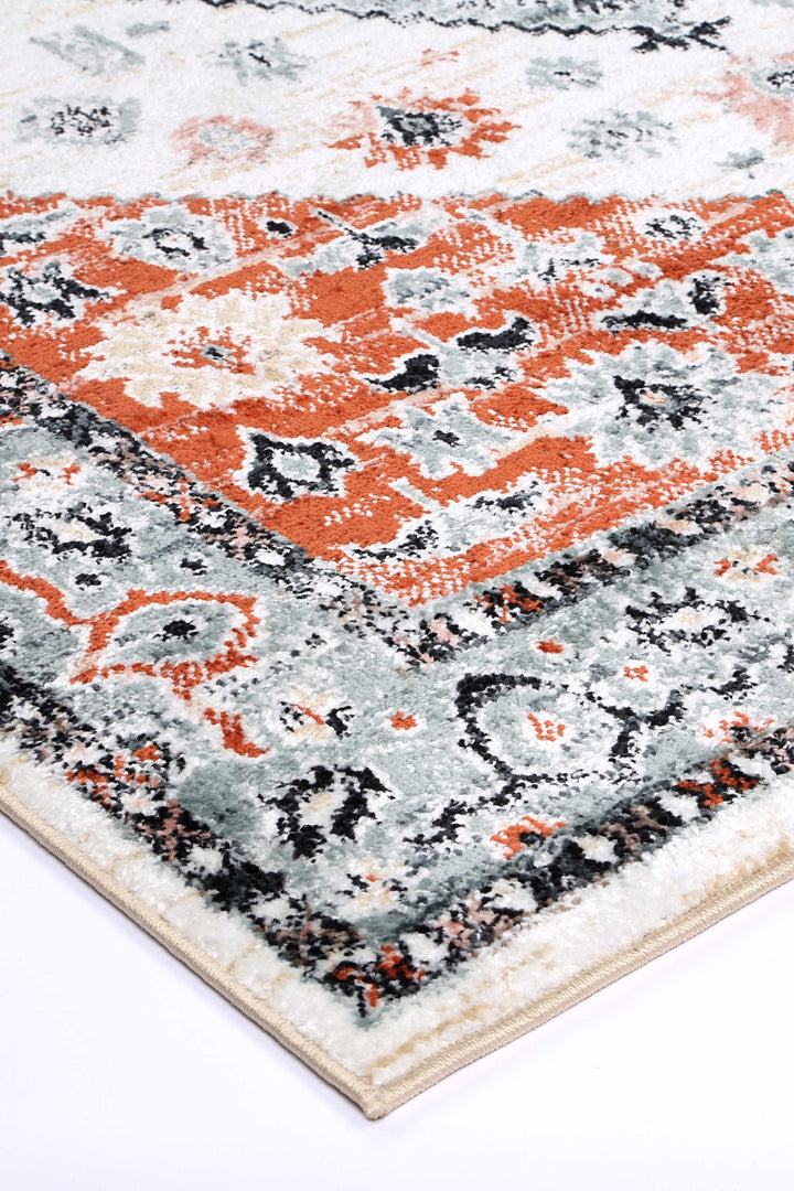 Corner of a patterned area rug with orange, grey, and black geometric motifs