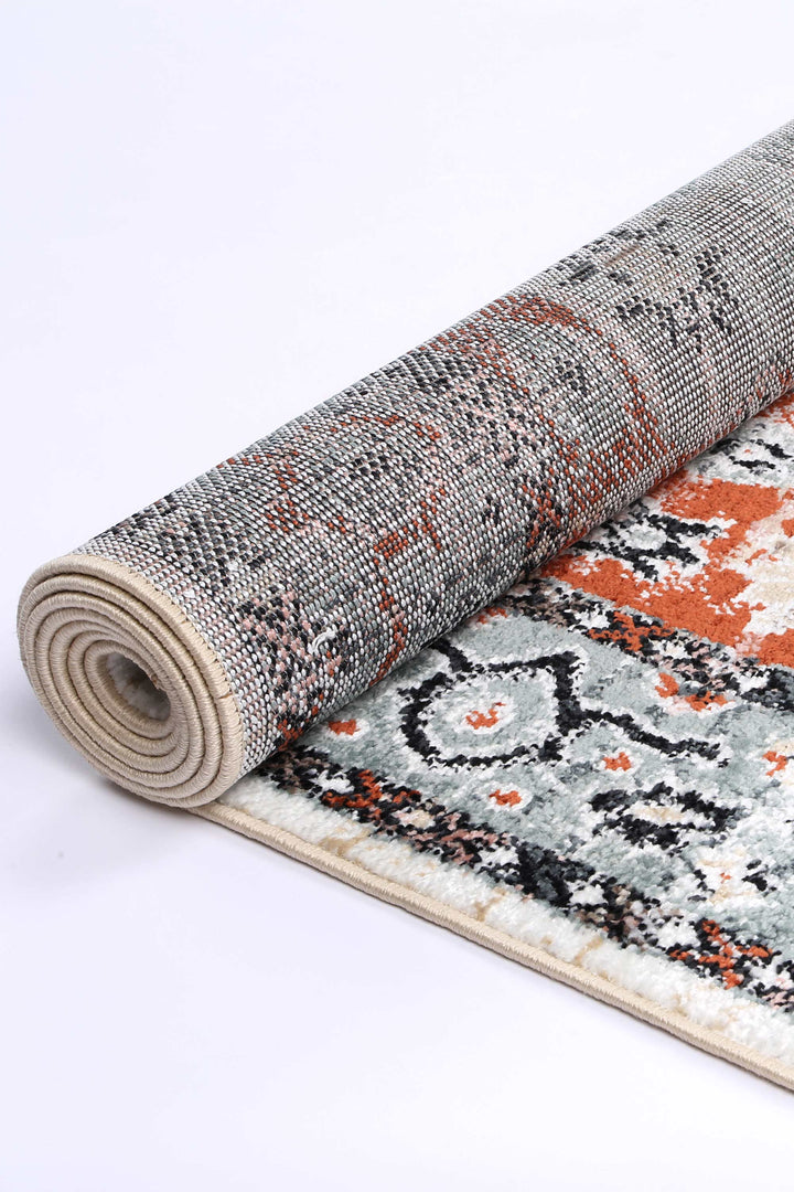 Rolled area rug with abstract orange, black, and cream pattern on white background