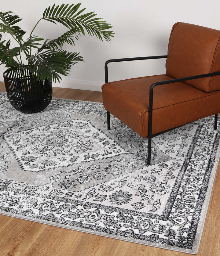 Modern living room with brown accent chair, grey patterned rug, and potted plant on wood floor