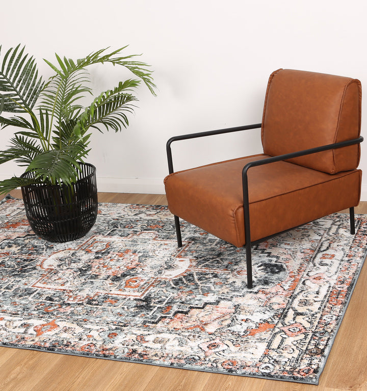 Modern brown leather accent chair with black metal frame on patterned area rug, next to potted plant