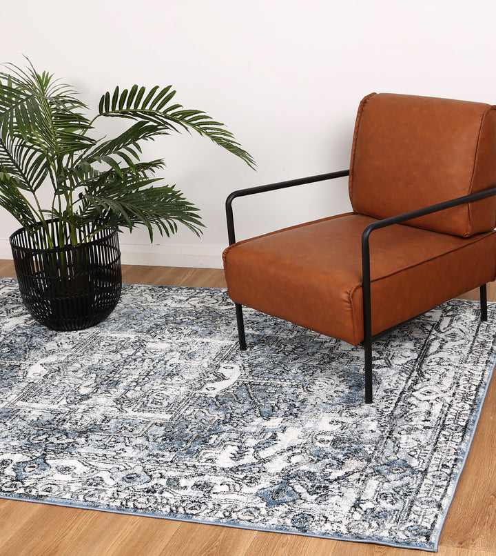 Modern brown accent chair on blue and white patterned rug with potted plant in living room