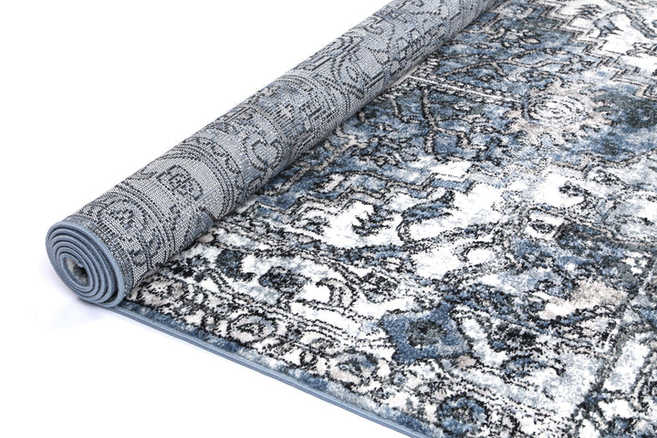 Blue and white area rug with intricate pattern, partially rolled on a white background