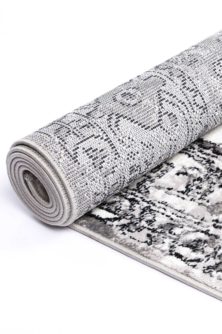 Rolled grey area rug with abstract black and white pattern, soft texture, close-up view