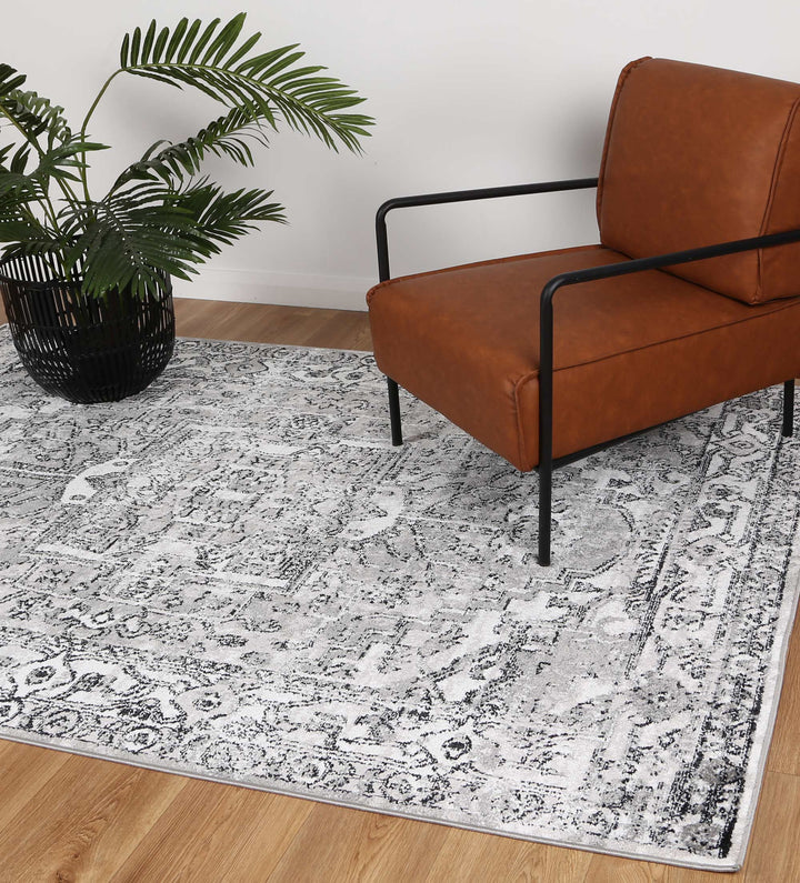 Modern living room with grey patterned area rug, brown accent chair, and potted plant on wood floor