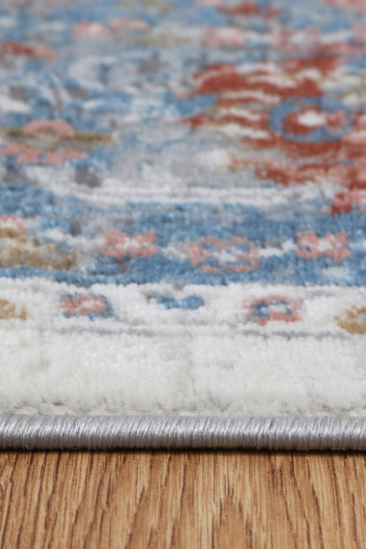 Closeup of a colorful patterned area rug with blue, red, and cream tones on wood floor