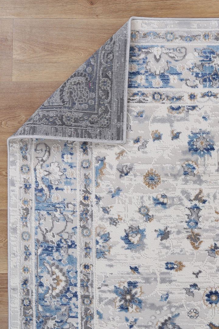 Blue and grey floral area rug with corner flipped on wooden floor
