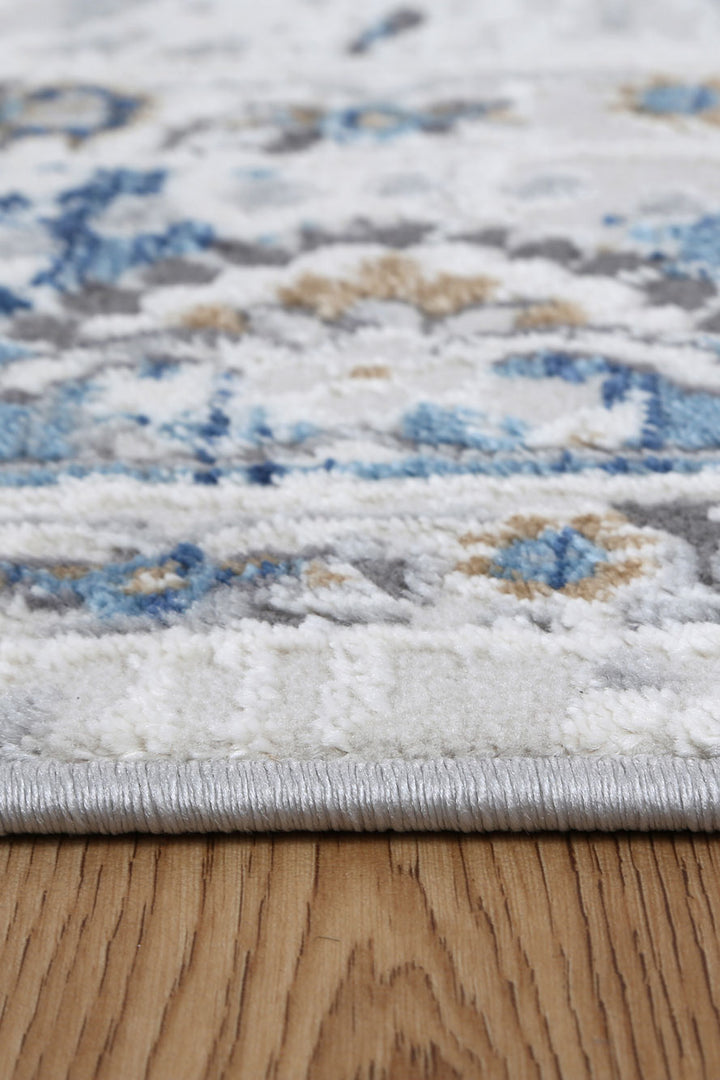 Close-up of a patterned area rug with blue, beige, and gray accents on wooden floor
