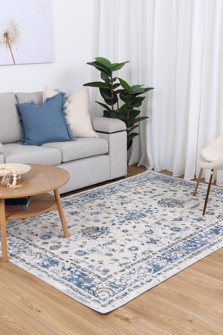 Modern living room with light grey sofa, blue accent pillows, wooden coffee table, and blue patterned area rug on wood flooring