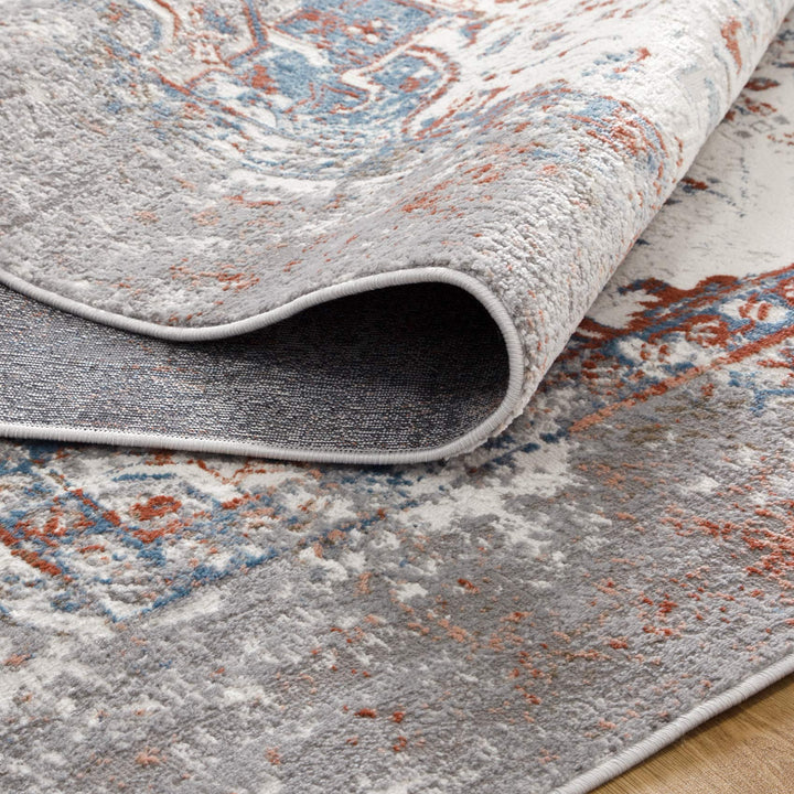 Close-up of a modern area rug with distressed gray, blue, and rust patterns on wood floor