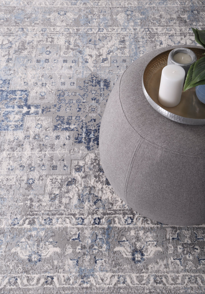 Blue and grey patterned rug with round grey ottoman and decorative tray