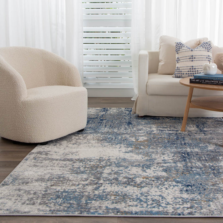 Modern living room with a cream accent chair, beige sofa, blue abstract area rug, and wood coffee table