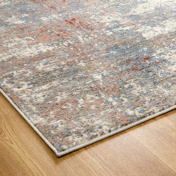 Modern area rug with abstract pattern in grey, blue, and orange on wooden floor