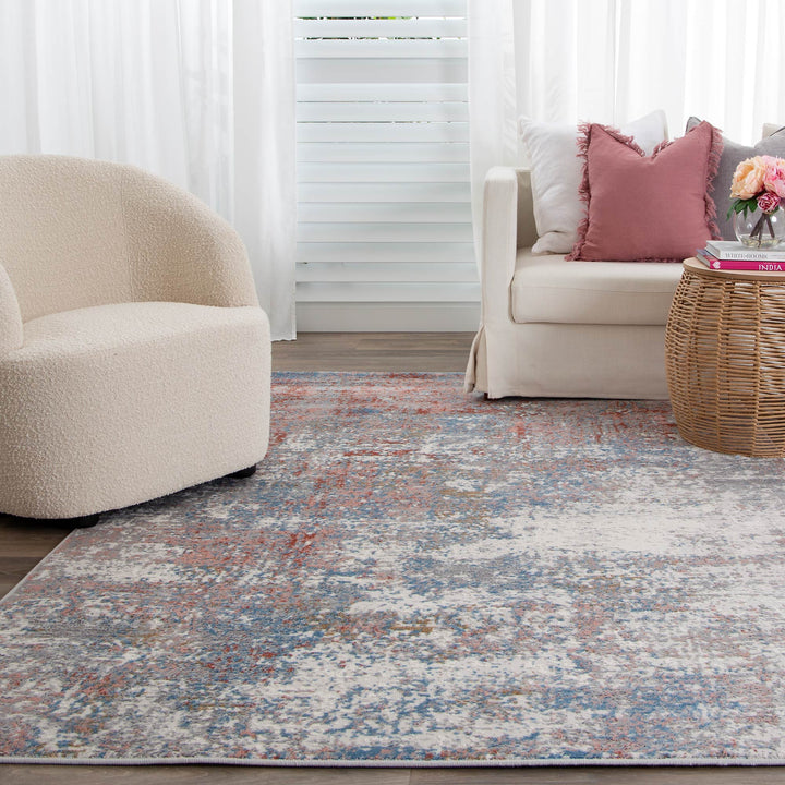 Modern living room with a cream accent chair, white sofa, pink pillows, and a patterned area rug.