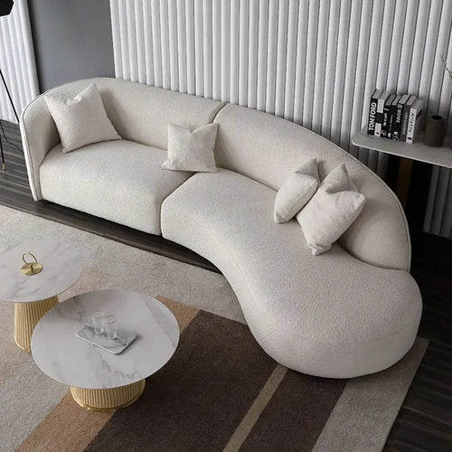 Modern curved beige sofa with matching pillows, marble coffee tables, and striped rug in contemporary living room