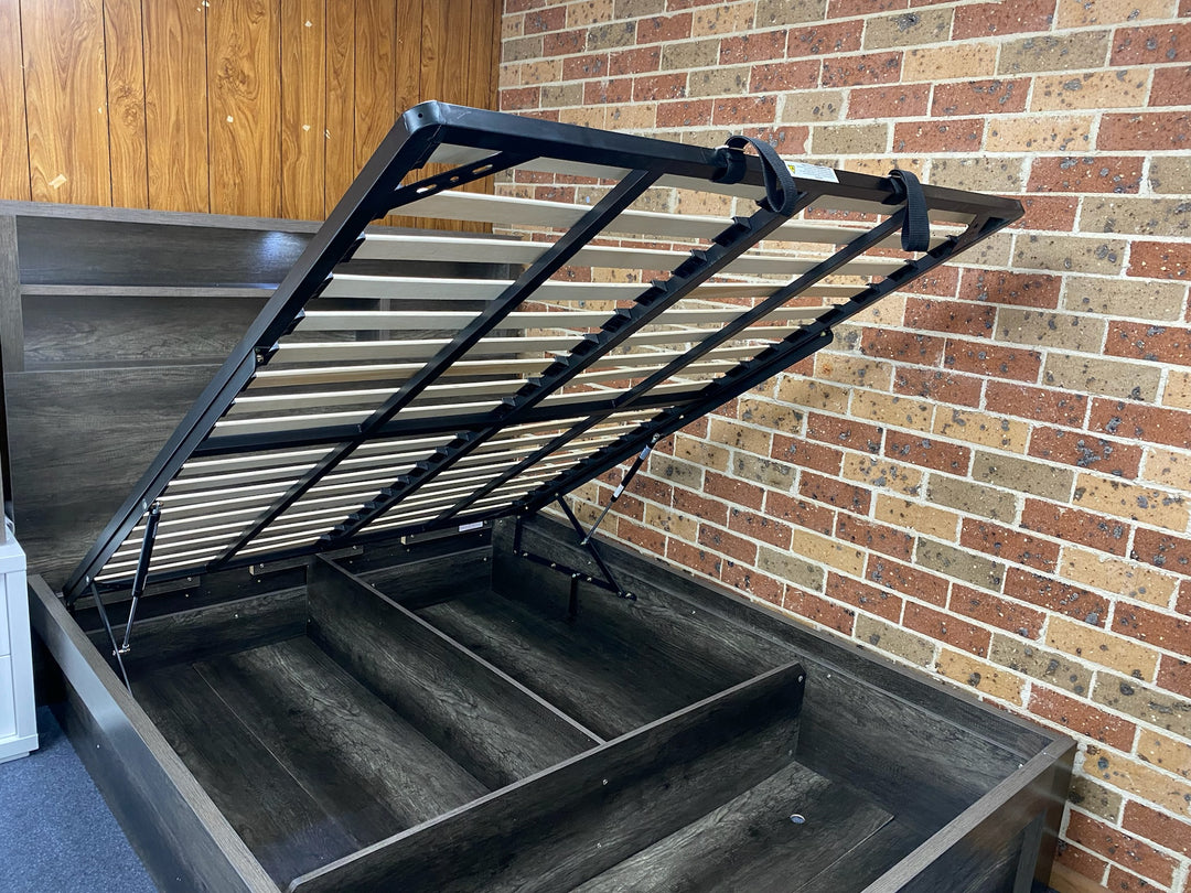 Lift-up storage bed frame with hydraulic mechanism against brick and wood panel walls