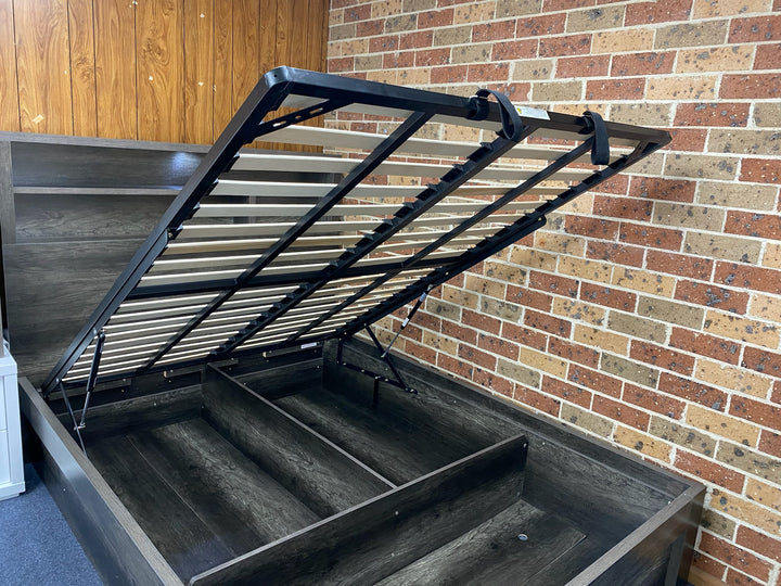 Lift-up storage bed frame with hydraulic mechanism against brick and wood panel walls