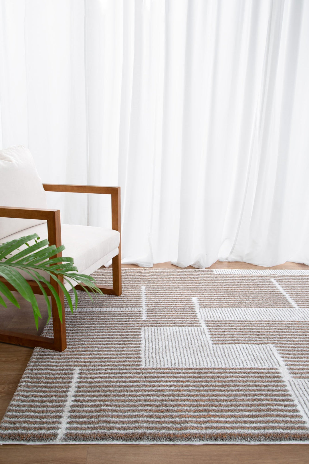 Modern geometric area rug with neutral tones, next to a wooden armchair and green plant