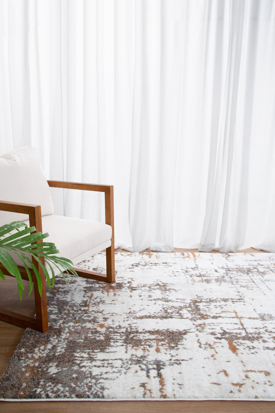 Modern living room with white cushioned wooden armchair, patterned area rug, and sheer curtains