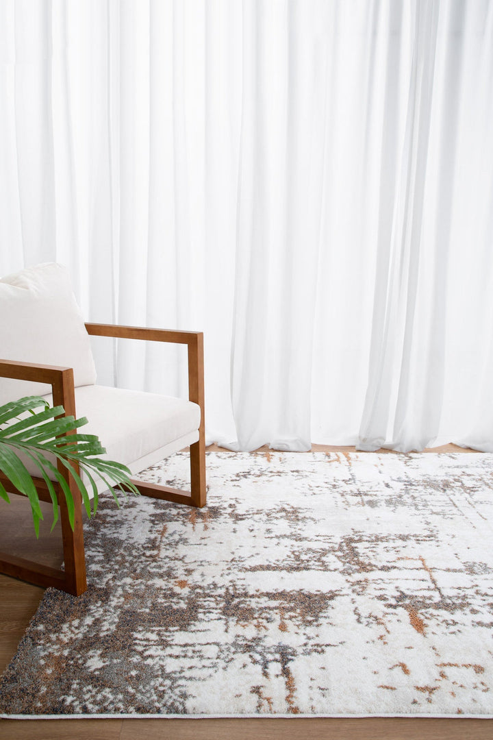 Modern living room with white cushioned wooden armchair, patterned area rug, and sheer curtains