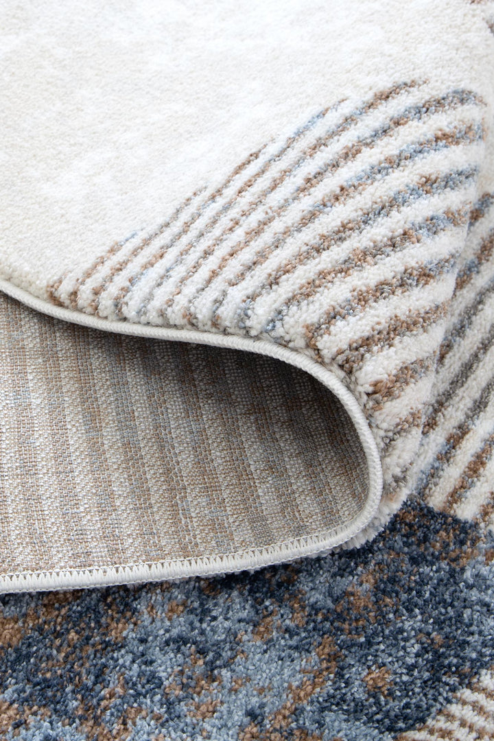 Close-up of a modern area rug with cream, blue, and beige textured stripes and woven backing