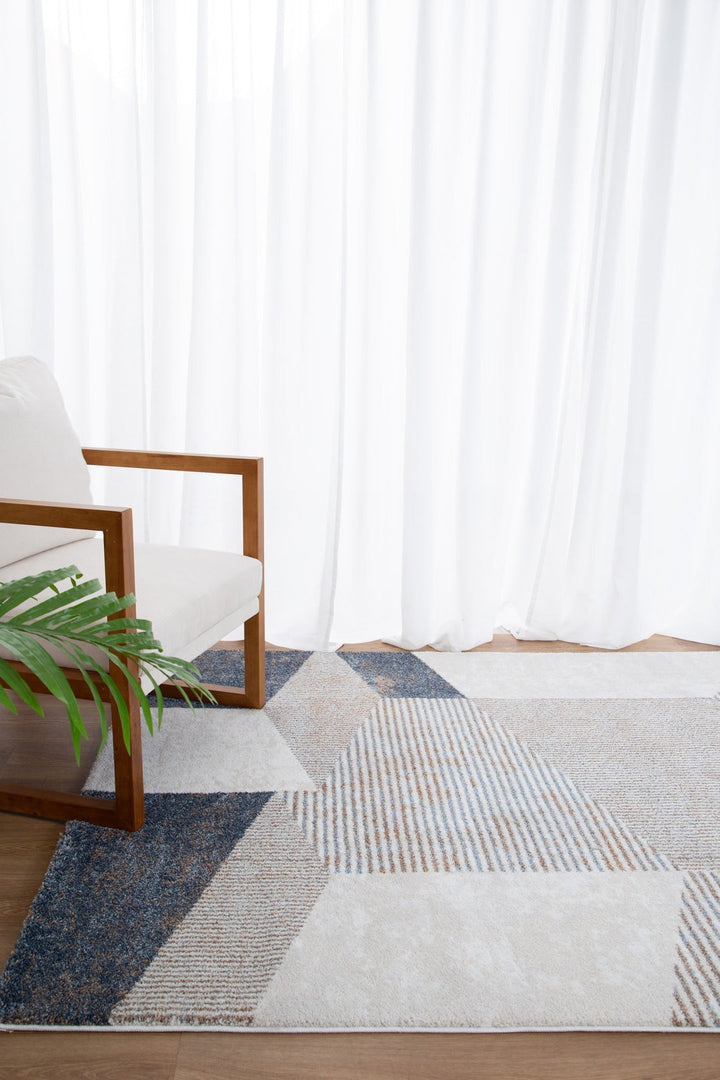 Modern armchair with wooden frame, geometric patterned area rug, white curtains, and green plant in a bright living room