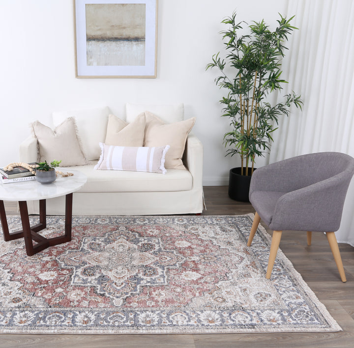 Modern living room with beige sofa, gray accent chair, patterned area rug, and potted plant