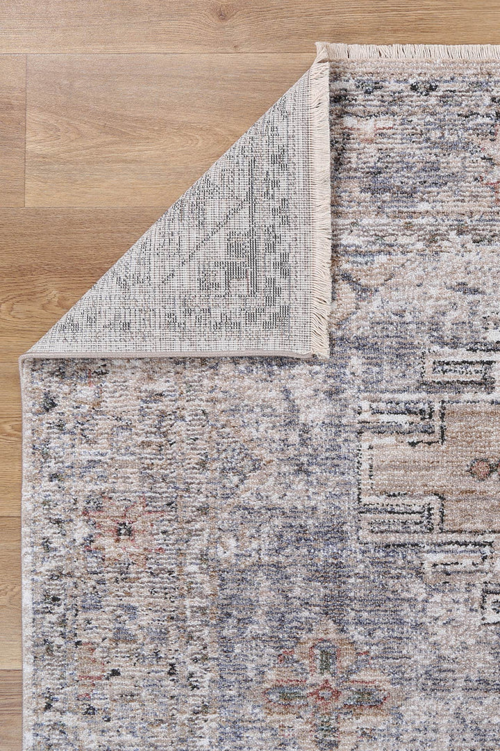 Vintage patterned area rug with muted colors on wooden floor, corner flipped to show backing.