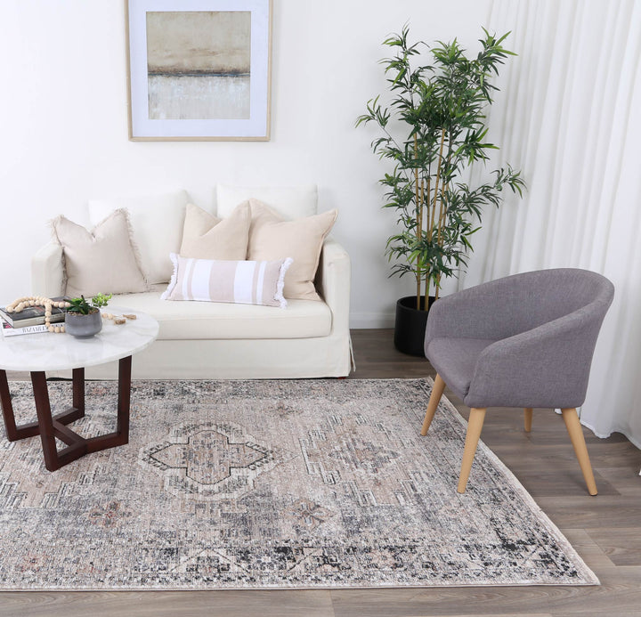 Modern living room with beige sofa, gray accent chair, patterned rug, marble coffee table, indoor plant, and wall art