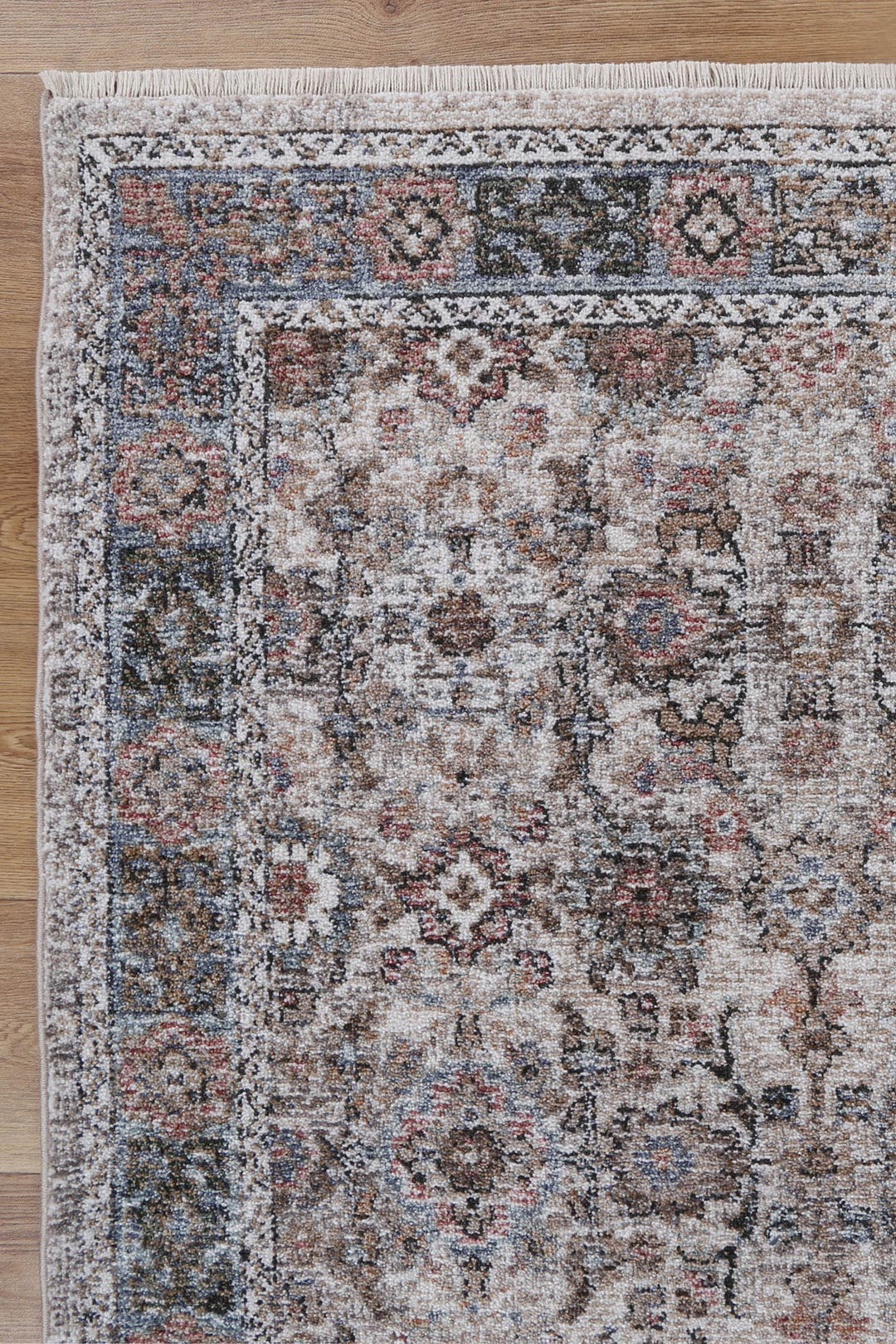 Corner of a beige and blue vintage-style area rug with intricate floral patterns on wood floor