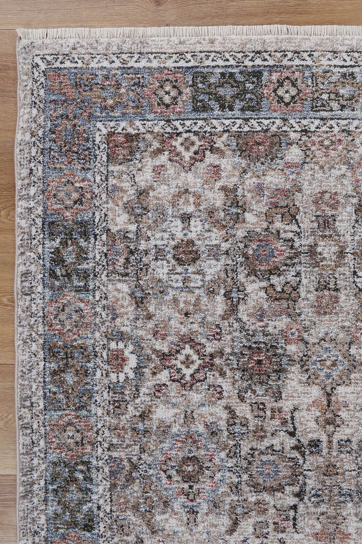 Corner of a beige and blue vintage-style area rug with intricate floral patterns on wood floor